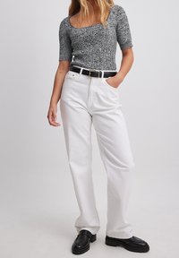 Top grigio a maniche corte lavorato a maglia con scollatura quadrata, abbinato a pantaloni di jeans bianchi a vita alta e una cintura nera. Scarpe in pelle nere.