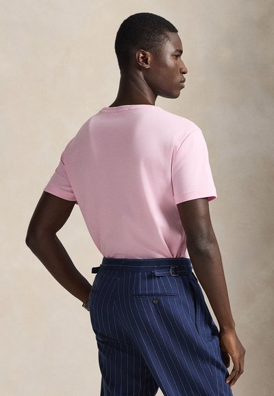 Rausvo atspalvio trumpomis rankovėmis marškinėliai su apvalia apykakle, derinami su tamsiai mėlynomis dryžuotomis kelnėmis su diržo kilpelėmis ir šoninėmis kišenėmis.