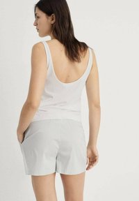 Witte mouwloze top met een lage rug, gecombineerd met lichtgrijze gestreepte shorts met zijkanten en een relaxte pasvorm.