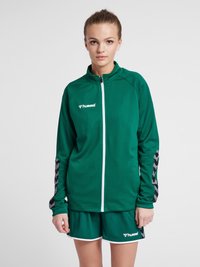 Groene sportjack met rits aan de voorkant, textuurstof en gestreepte zwart-grijze accenten op de mouwen, gecombineerd met bijpassende shorts.