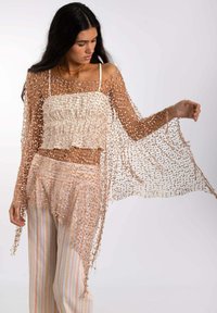 Top de ganchillo ligero, de punto abierto, color beige, con mangas largas y un dobladillo asimétrico en capas. Combinado con pantalones de pierna ancha a rayas.