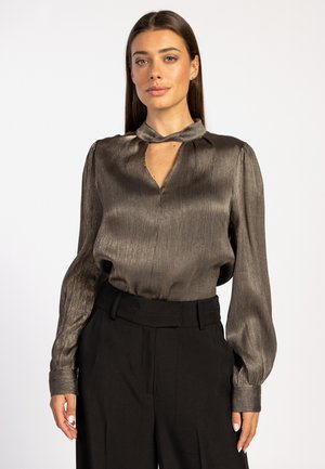 Donker metallic blouse met een krawatkragen, lange puffmouwen en een keyhole-halslijn. Draagt met hoge, zwarte broeken. Nette structuur.