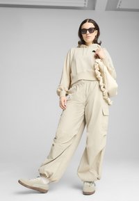 Beige cropped hoodie met trekkoord, loszittende beige cargobroek met zakken en beige sneakers met bruine zolen. Inclusief een gerimpelde tas.