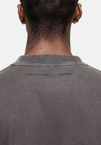 Grijze katoenen t-shirt met een ronde hals, met een subtiele handtekening detail op de achterkant en een soepele textuur.