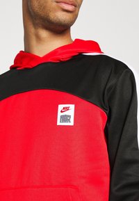 Sweat à capuche Nike Force en rouge et noir, doté d'une poche kangourou, d'un tissu texturé, d'un écusson logo brodé et d'accents blancs contrastants.