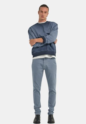 Felpa blu navy con sfumature di blu più chiaro, collo rotondo e polsini a coste, abbinata a jeans azzurri e stivaletti neri alla caviglia.