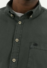 Camicia button-up verde scuro in cotone, con colletto a punta, bottoni color crema e taschino con ricamo del logo nero.