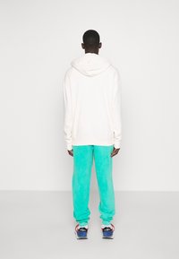 Vit hoodie med dragsko, tillsammans med ljus turkosa joggers. Joggers har en mjuk textur och elastiska muddar. Sportskor fulländar looken.