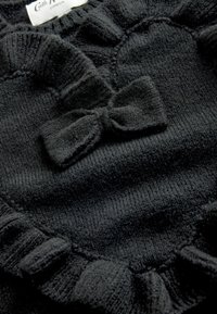 Svart stickad tröja med ett hjärtformat mönster, volangkanter och en central rosettaccent; mjukt material med ribbdetaljer.