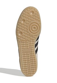 Semelle de chaussure en caoutchouc beige texturé, présentant un motif circulaire et en diamant, avec des rayures noires sur le côté et le branding Adidas.