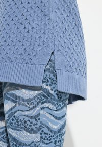 Ljusblå stickad tröja med en strukturerad diamantmönster och ribbad fåll, med sidospalter. I kombination med mönstrade blå byxor i vågor och linjer.