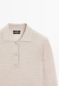 Jasnobeżowa wełniana koszulka polo z płaskim kołnierzem, trzema guzikami i fakturowaną tkaniną. Metka mówi "Massimo Dutti, 100% wełna."