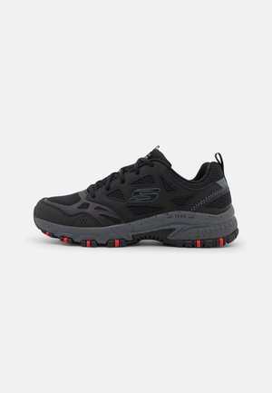 Las zapatillas de trail running negras cuentan con una parte superior de malla, suela de goma con acentos rojos y una entresuela acolchada para mayor comodidad y agarre.