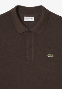 Tummanruskea polo-paita, jossa on kaulus, kaksi nappia ja Lacoste-logo vasemmassa rinnassa. Yksinkertainen ja tyylikäs muotoilu.