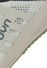Light grey athletic shoe featuring a mesh upper with textured accents, a solid rubber sole, and "vibram sole system" embossed on the side.