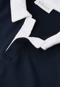 Tumši zils polo krekls ar baltu apkakli, ar teksturētu audumu, diviem pogu aizdari un etiķeti ar uzrakstu "PIEK-ONE". Mīksta kokvilnas materiāls.