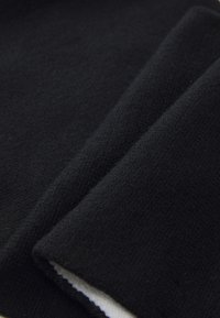 Sort sweaterstof med en blød tekstur, hvor foldede sektioner viser en glat overflade og subtile stingdetaljer.