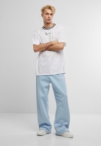 White short-sleeve t-shirt with black collar details and front logo, paired with light blue wide-leg sweatpants and white sneakers.