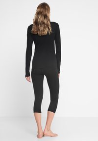 Schwarzes Langarmshirt mit einer figurschmeichelnden Passform, kombiniert mit schwarzen, knöchellangen Leggings. Beide Kleidungsstücke sind glatt und dehnbar, ideal für Sportbekleidung.
