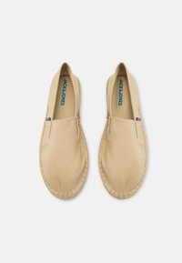 Beige lærred slip-on sko med syede kanter og et let espadrille design. Har et blåt logo på indersålen.