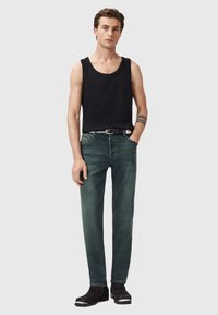 Černý top na ramínka, zelené džíny a černé kotníkové boty se stříbrnými akcenty. Úzký střih s neformálním stylem, obsahující pásek a kapsy.