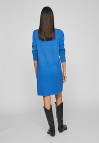 Abito blu lavorato a maglia con maniche lunghe, polsini e orlo a coste. Abbinato a stivali neri al ginocchio. Texture morbida e design che arriva fino al ginocchio.