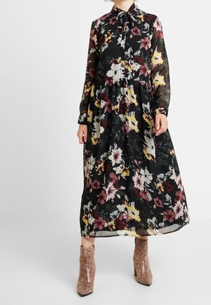 Long-sleeve, black floral dress with a collar, featuring multicolored flowers, a gathered waist, and transparent fabric. Paired with ankle boots.