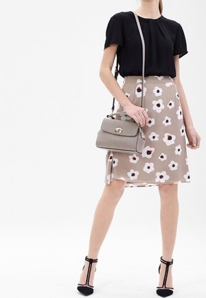 Blusa nera, gonna floreale beige con accenti bianchi e rossi, borsa grigia, scarpe con tacco nero con cinturini alla caviglia.