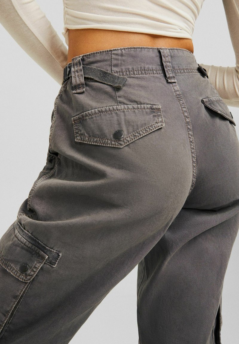 Grijze cargobroek met een relaxte pasvorm, voorzien van achterzakken, zichtbare stiksels en een gladde textuur. Materiaal is katoen of een vergelijkbare stof.