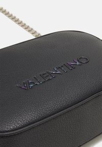 Černá kožená crossbody taška s texturovaným povrchem, která obsahuje iridescentní logo "VALENTINO" a stříbrný řetězový popruh.