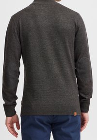 Tummanharmaa neulottu villapaita, jossa on korkea kaulus, resorireunaiset hihat ja kyynärpääpaikat; villapaidassa on teksturoidun näköinen pinta ja pieni logopilkku helmassa.