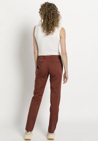 Kalhoty v rezavé barvě s rovný fit, obsahující dvě zadní kapsy a decentní detaily šití. Vyrobeny z hladké směsi bavlny.