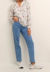 Blomstret bluse i lys pink og grøn med v-udskæring, parret med højtlivet blå jeans og hvide sneakers med sorte detaljer.