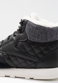 Svart vadderat lädersneaker med grå ullkrage och vit fleecefoder, med svarta och vita snören samt vit gummisula.