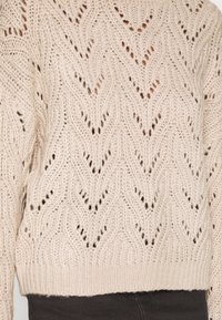 Gebreide trui in lichtbeige met een chevronpatroon. Heeft een ronde halslijn en geribbelde zoom. Gemaakt van gestructureerd garen.