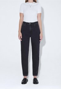 Svarta högmidjade jeans med avsmalnande ben, tillverkade av texturerad denim. Matchas med en åtsittande vit t-shirt och svarta slip-on skor.