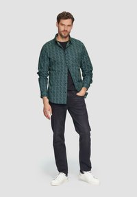 Groen patroon overhemd met knopen, zwarte t-shirt eronder, gecombineerd met donkere spijkerbroeken en witte sneakers. Ontspannen pasvorm met lange mouwen.
