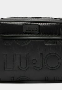 Melnas neilona soma ar reljefotu "LIU·JO" logotipu, ar rāvējslēdzēja aizdari un smalku izšūtu tekstūru. Kompakts dizains ar gludu apdari un minimālu aparatūru.