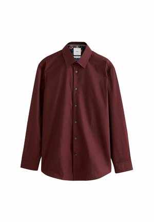 Hands adjusting the cuff of a long-sleeve maroon patterned shirt with black buttons.