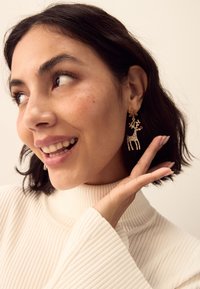 Gold-tone earrings featuring a reindeer design with crystal accents and a red nose, hanging from a snowflake top. Subtle texture throughout.