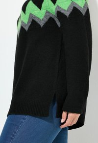 Černý pletený svetr s zelenošedým cikcak vzorem na výstřihu. Postranní rozparek a žebrované manžety pro texturu.