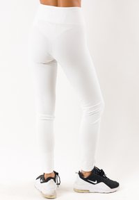 Leggings blancos con una cintura alta, con una textura suave. Combinados con zapatillas deportivas negras, mostrando una mezcla de estilos deportivos.