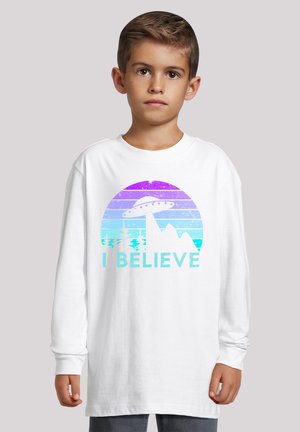 Langärmliges weißes T-Shirt mit einem lila-blauen Farbverlauf, der Berge, Bäume und ein UFO zeigt, mit dem Text "I BELIEVE" in Türkis.