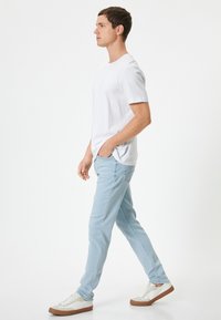 Vaqueros azul claro, camiseta de manga corta blanca y zapatillas casuales. Los vaqueros tienen un corte ajustado y bolsillos delanteros, con una textura suave.