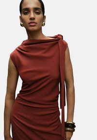 Rostfarbenes Kleid mit drapierter Stoffgestaltung, ärmellosem Design und Krawattendetail an einer Schulter. Glatte Textur, figurbetonte Silhouette und dezenter Glanz.
