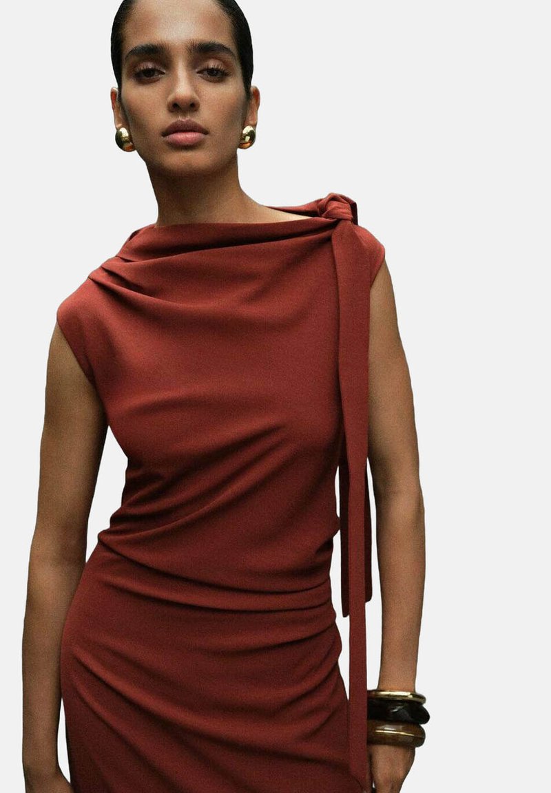 Rostfarbenes Kleid mit drapierter Stoffgestaltung, ärmellosem Design und Krawattendetail an einer Schulter. Glatte Textur, figurbetonte Silhouette und dezenter Glanz.