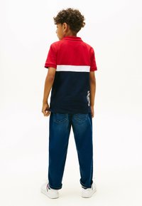 Rød og marineblå polo shirt med hvid stribe, korte ærmer og struktureret stof. Sammen med blå denim jeans og hvide sneakers.