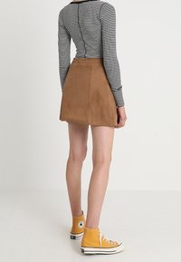 Bruine suède a-lijn rok met een gladde textuur, gecombineerd met gele high-top sneakers. Het bovenstuk heeft zwart-witte horizontale strepen.