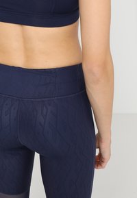 Marina träningsleggings med ett subtilt geometriskt mönster, hög midja och en slät yta, i kombination med en matchande sport-bh.