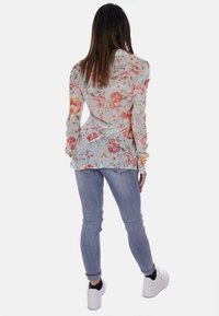 Blusa floreale a maniche lunghe in tessuto leggero e trasparente con una palette di colori pastello. Abbinata a jeans blu aderenti e sneakers bianche.